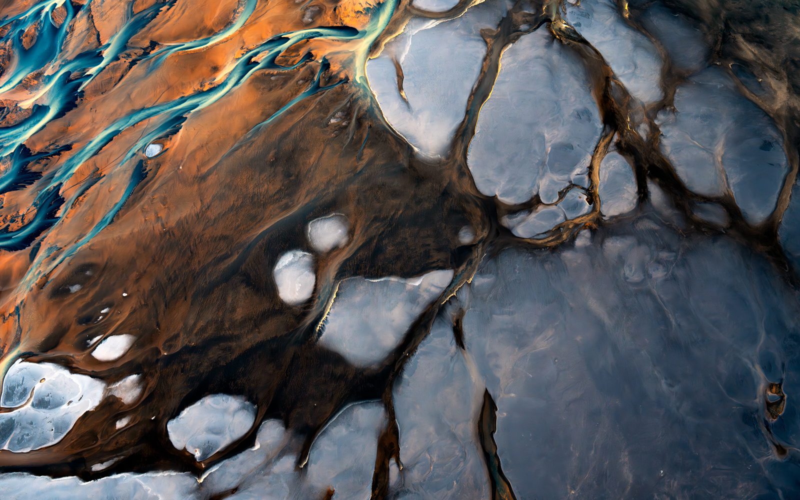 Turquoise braided channels across rust and black sand, from the air
