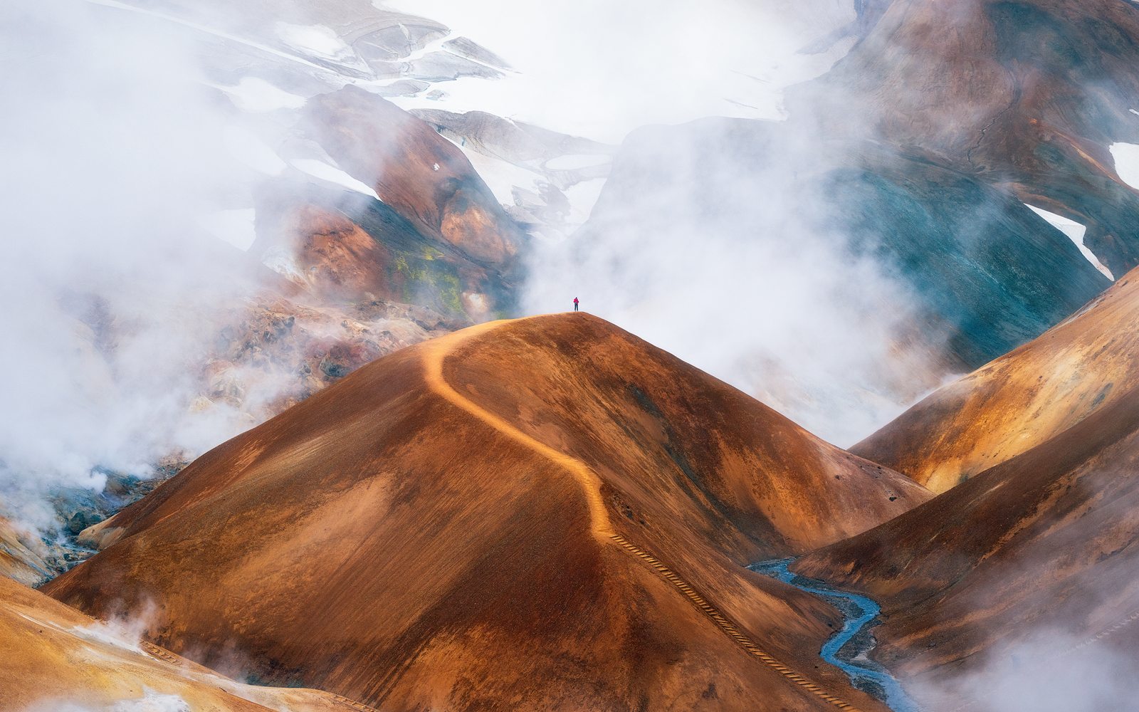 A lone hiker on a ridge between steaming hills